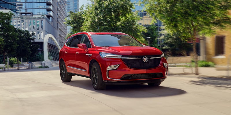 A red 2024 Buick Enclave driving down a city street on a sunny day