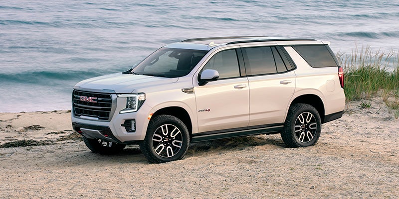 A pearl white 2024 GMC Yukon parked on the shoreline of a beach at dusk