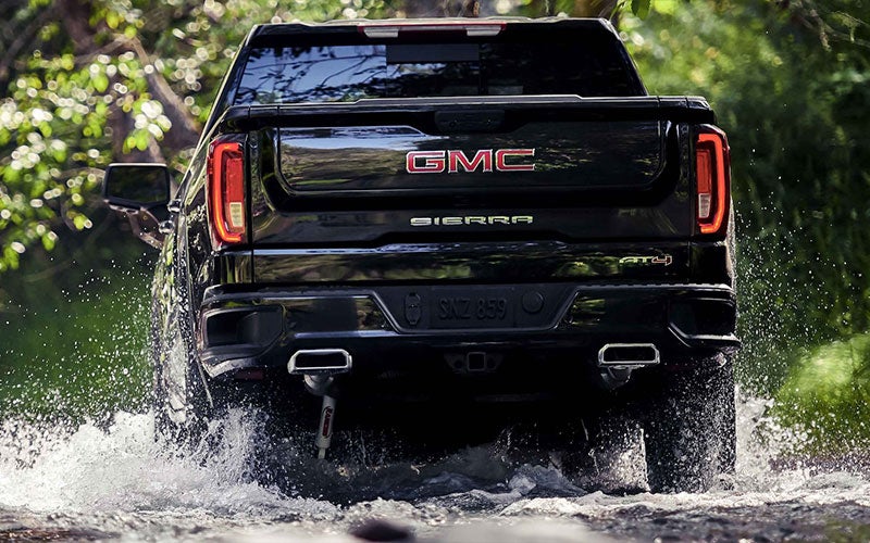 A black GMC Sierra driving through water on a sunny day with newly serviced shocks and struts