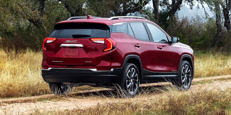 Rear view of a red 2024 GMC Terrain driving through tall grass